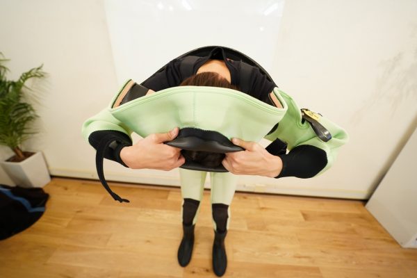 女性スタッフがドライスーツを頭から着る様子