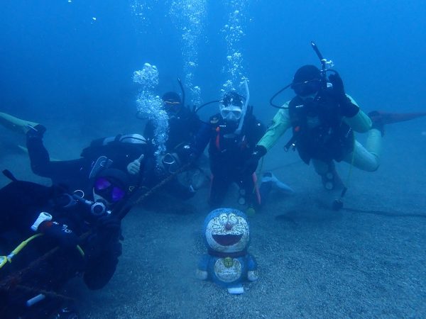 江之浦の海の中でドラえもんと一緒に記念写真を撮る5人のダイバー