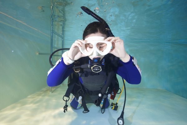 プールの水中でマスクに水を入れる女性ダイバー