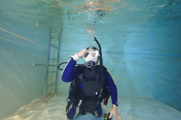 プールの水中でマスクから水を抜く女性ダイバー