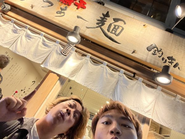 ラーメン屋の前で写真を撮る男性2人